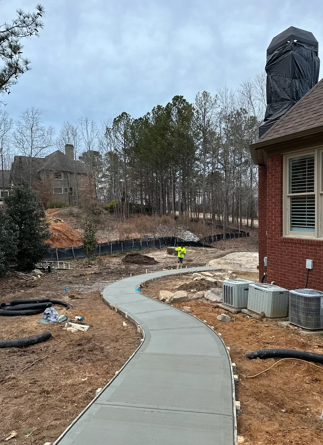 Curved concrete walkway with drainage pipe and graded soil on residential property