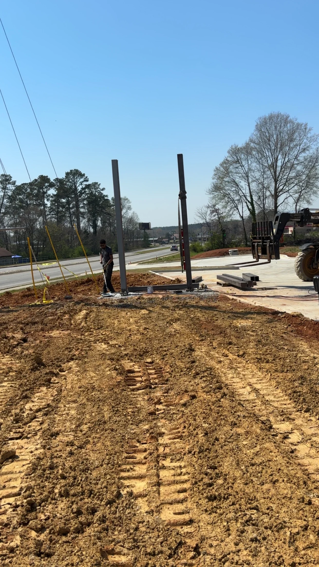 Two steel posts installed in concrete footings with yellow bracing on prepared dirt foundation